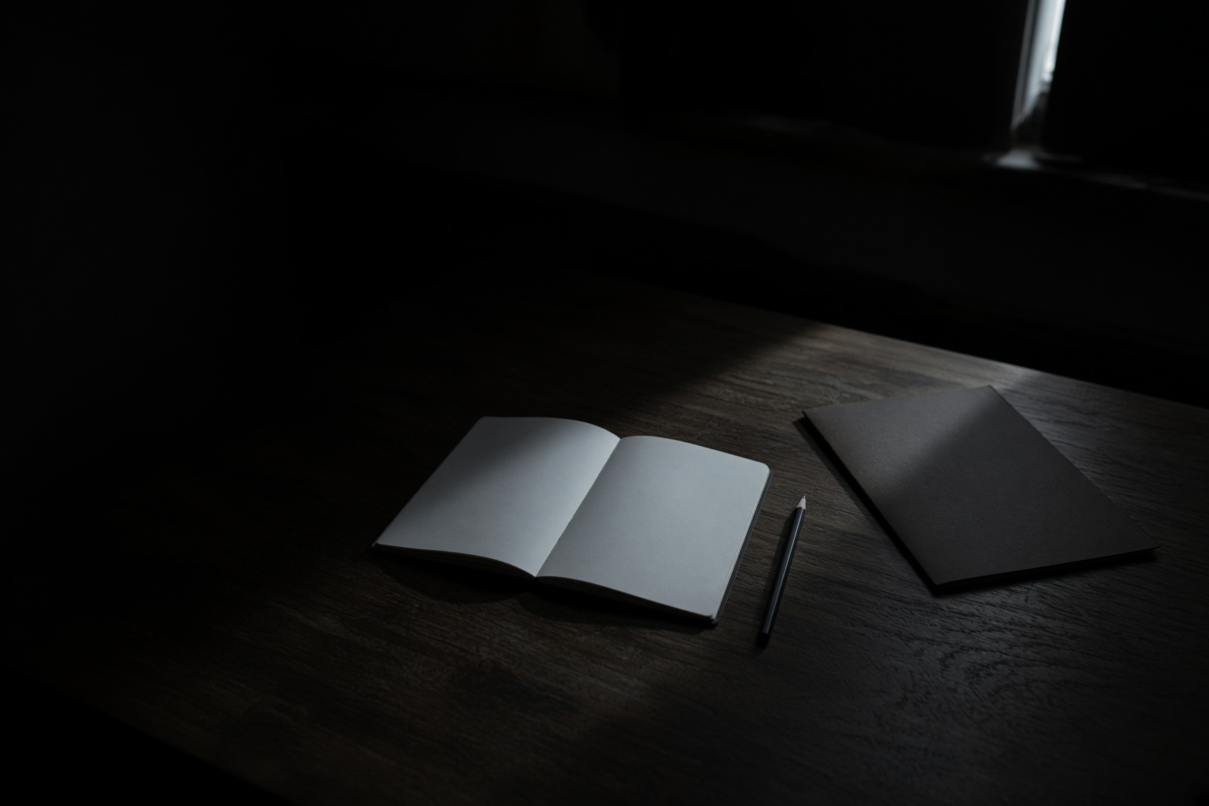 A blank notebook and a pencil on a dark table, crossed by a narrow band of dawn light.